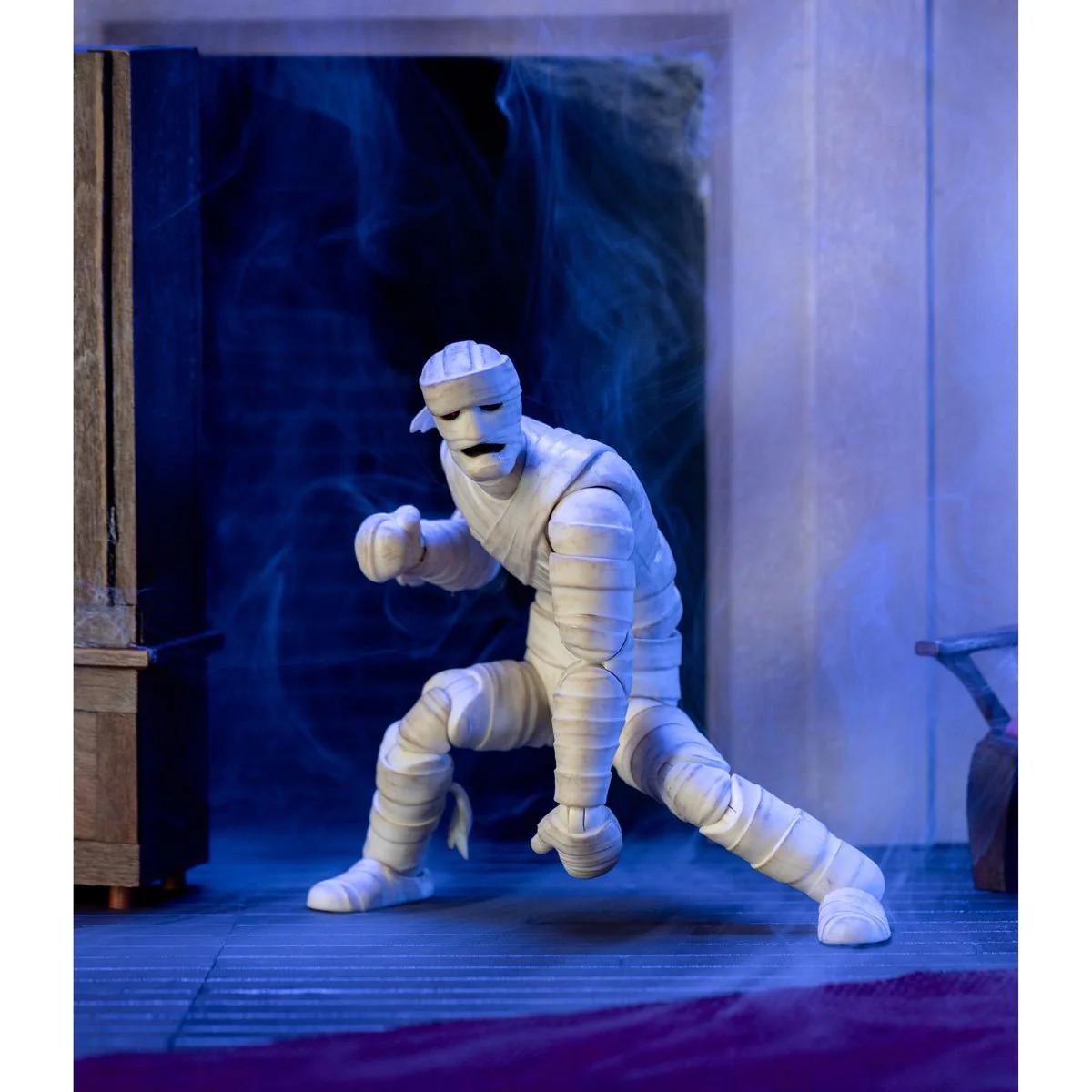A detailed action figure of the Mummy of Ankha from Scooby-Doo, posed with one fist raised, showcasing intricate bandaging and a ghostly background.Jada Scooby-Doo Wave 1 Mummy of Ankha
